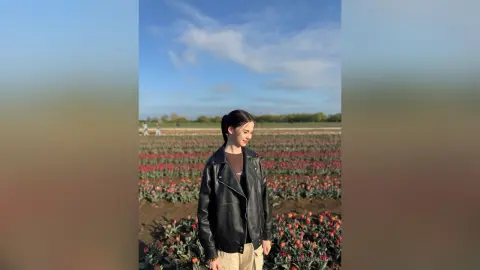 Young woman in a black leather jacket standing in a blooming red tulip field under a blue sky.