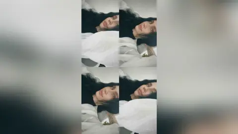 SofiMils lying in bed with her long dark hair spread out, wearing a white top or sheet covering her body.