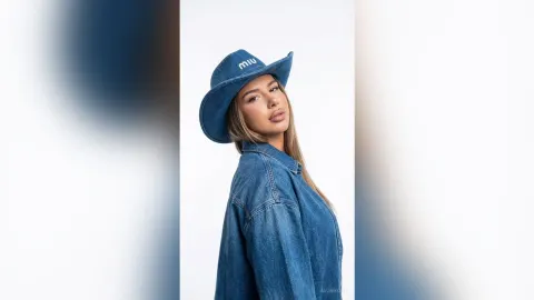 AvaBronX — AvaBronX wears a blue denim hat and an oversized denim shirt while posing against a white background.
