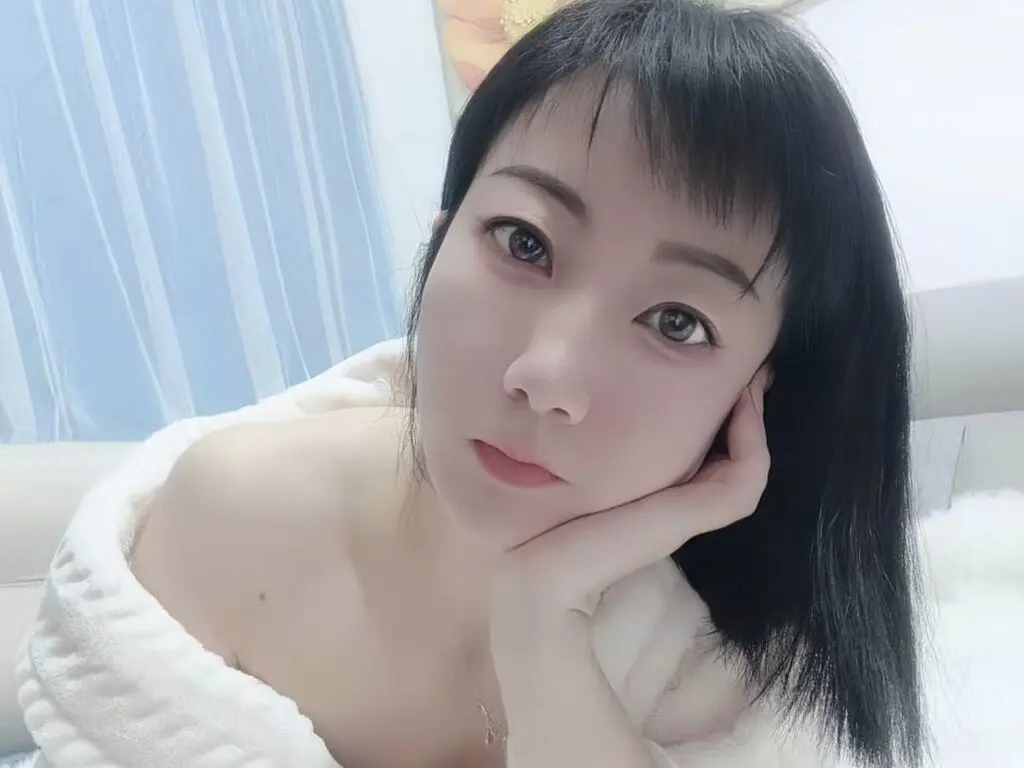 Young woman with dark hair in a white cozy robe relaxing on a bed in a bright bedroom.