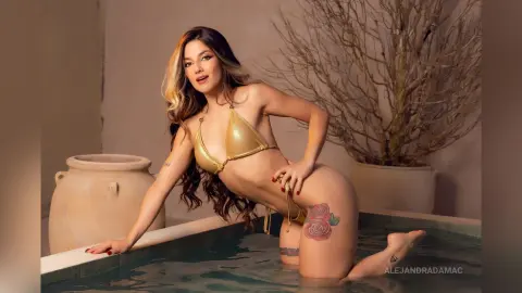 Woman in a gold bikini relaxing in a luxury indoor pool next to a large ceramic vase and decorative branches.