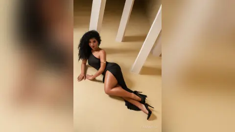 Elegant woman in a sleek black cocktail dress posing on a minimalist beige staircase with a sophisticated mood.