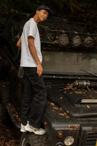 KylePresly stands beside a black off-road vehicle wearing a white t-shirt and black cargo pants.