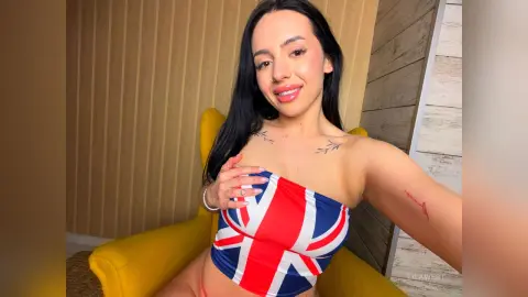 Smiling woman in a Union Jack tube top sitting on a yellow chair in a modern room.