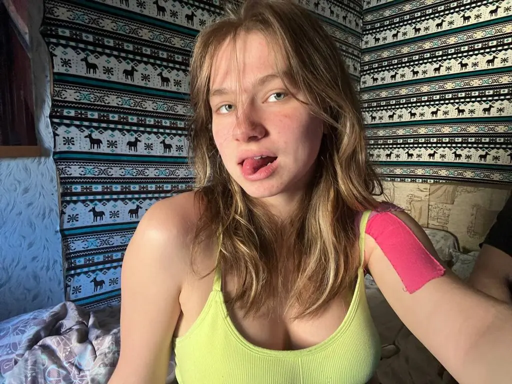 Young woman in a lime green tank top sitting in a room with patterned bohemian wall hangings.