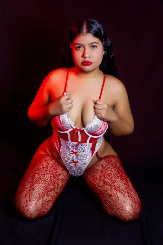 NataliEvansx poses in red and white lace lingerie and red lace stockings against a dark background.