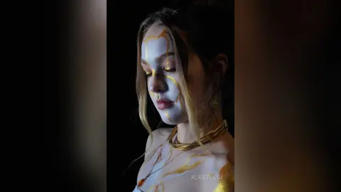 AliceTucci poses with gold paint dripping down her face and chest, wearing a thick gold neck ring against a dark background.