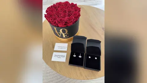 Romantic gift set featuring a box of red roses, silver earrings, and a personalized thank you note on a wooden table.