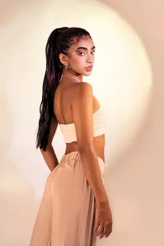Veronica_Hottiee poses sideways in a cream-colored tube top and matching skirt, showing her long dark hair in a high ponytail.