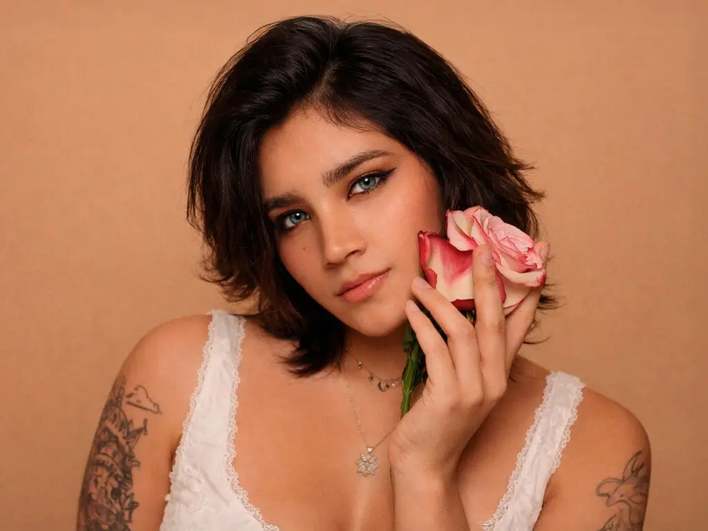 Young woman in a white lace camisole holding a pink rose against a warm beige background with a soft romantic mood.