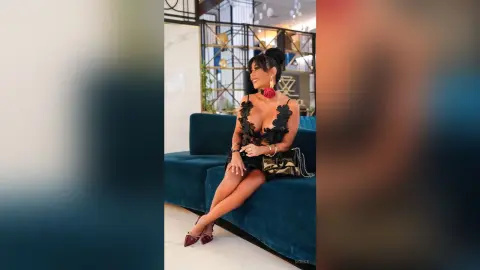 Dolce sits on a blue velvet sofa wearing a black lace plunging neckline dress and red heels.