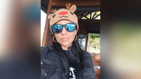 Woman in a reindeer hat and sunglasses wearing a black puffer jacket outdoors in a festive mood.