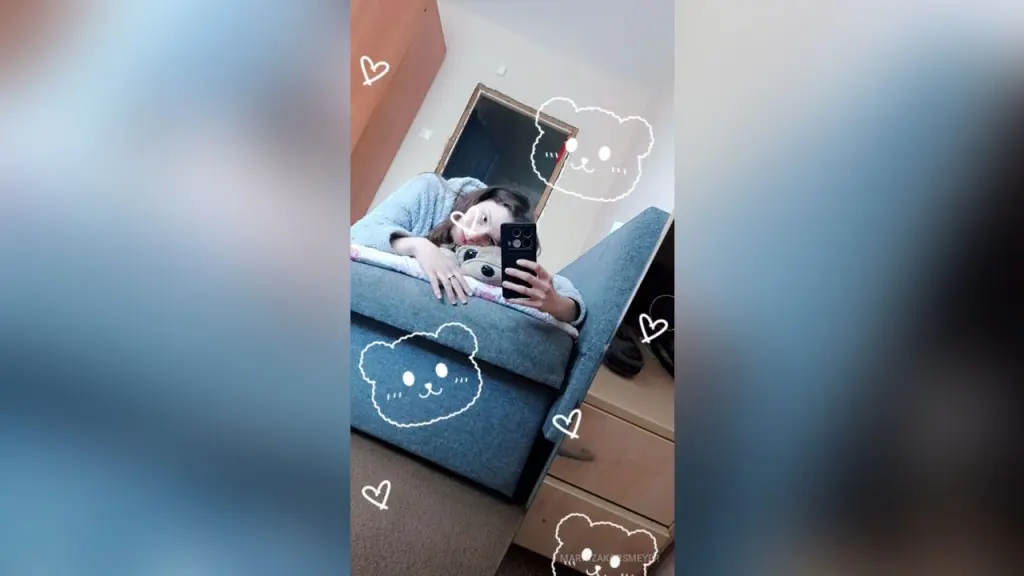 Young woman in a black sweatshirt taking a playful mirror selfie with a kissy face expression.