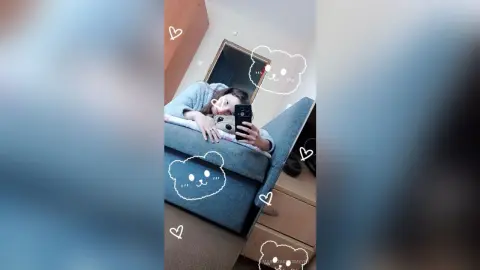 Young woman in a grey sweater relaxing on a blue sofa in a cozy bedroom setting.