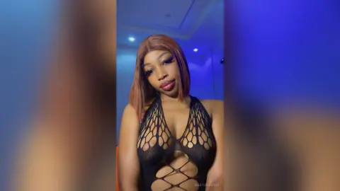 Glamorous woman in a black cutout mesh bodysuit posing under moody blue lighting.