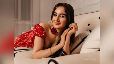ElizabethMeyer smiles while lying on a white chair wearing a red polka-dot dress with her hands near her face.
