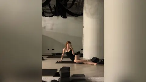 AlbertaCorrell is a redhead in a black bodysuit posing on a yoga mat in a bright studio.