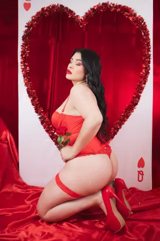 Woman in red lace lingerie kneeling before a large heart backdrop for a romantic Valentine's Day photoshoot.