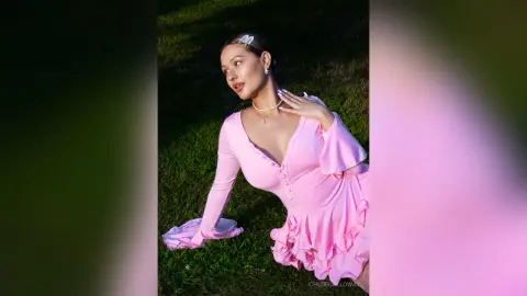 Elegant woman in a pink long-sleeve ruffled dress posing outdoors in soft sunlight.
