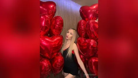 MarryDavies poses in a black bodysuit surrounded by large red heart-shaped balloons.