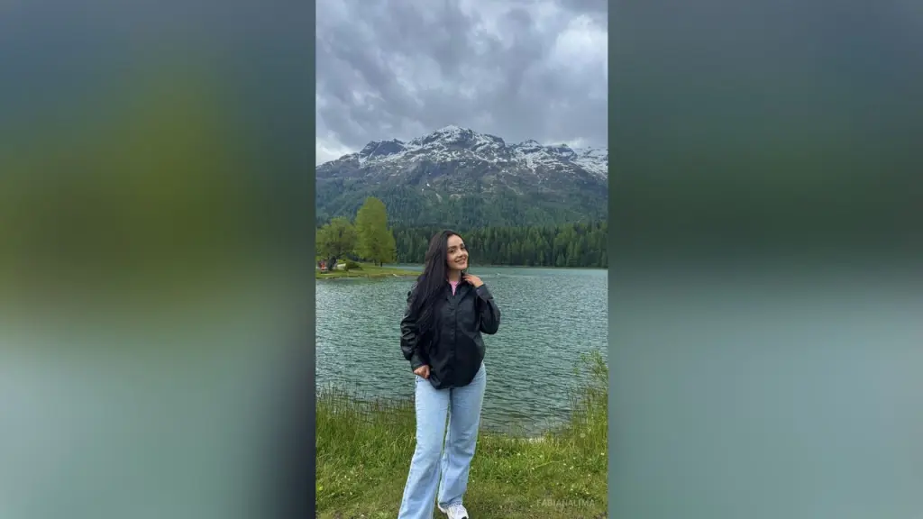 FabianaLima — FabianaLima stands in a grassy field by a lake with snow-capped mountains in the background, wearing a black button-down shirt and light blue jeans.