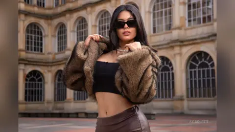Stylish woman in a brown faux fur jacket and black crop top posing in front of classic European architecture.