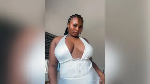 Confident Black woman in a white plunging halter dress posing in a bright indoor setting.