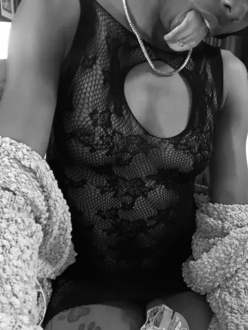 Woman in a black lace cutout bodysuit and silver necklace posing playfully in a cozy sweater.