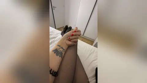 Woman in sheer black tights and dark shoes relaxing on a white bed in a bright minimalist bedroom.