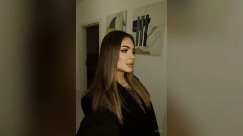 Elegant woman with long brown hair in a black outfit posing in a modern minimalist room.