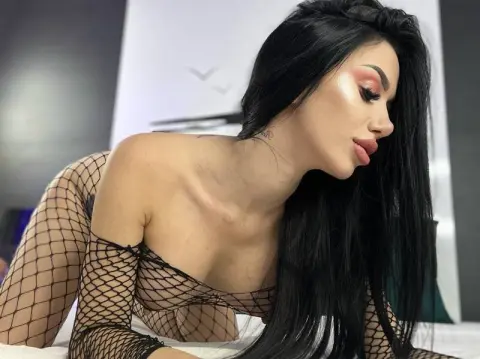 Glamorous woman with long black hair wearing a black fishnet bodysuit in a bright studio setting.