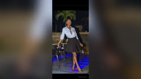 Elegant woman in a blue striped shirt and black mini skirt posing outdoors at night under palm trees.
