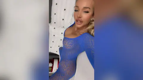 Young woman in a blue lace long-sleeve bodysuit posing in a bright indoor setting.