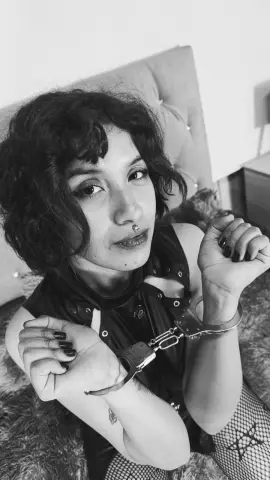 Moody black and white portrait of a woman in a dark sleeveless top and fishnet tights wearing handcuffs.