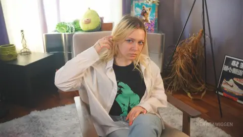 Blonde woman in a white shirt and black graphic tee relaxing in a cozy, sunlit living room.