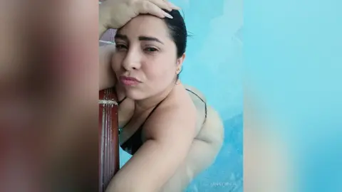 Young woman in a black bikini relaxing by a bright blue swimming pool on a sunny summer day.