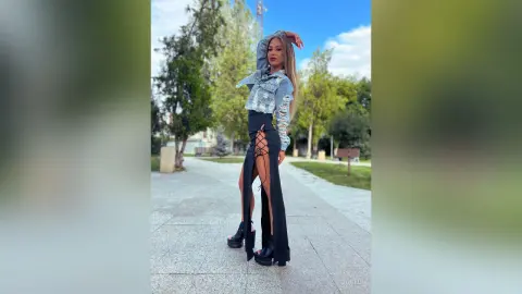 Stylish woman in a denim jacket and black lace-up maxi skirt posing on a sunny outdoor walkway.