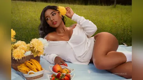 Beautiful Black woman in a white off-the-shoulder top relaxing on a picnic blanket with yellow flowers.