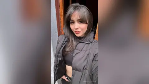 Young woman with long brown hair wearing a black puffer jacket standing outdoors in a casual mood.