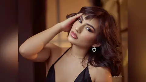 Glamorous woman with wavy brown hair and heart earrings posing in a black halter top with soft lighting.