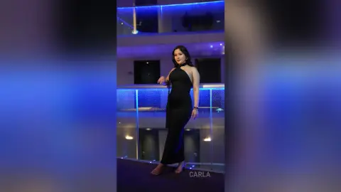 Elegant woman in a sleek black halter dress posing on a modern balcony with moody blue lighting.