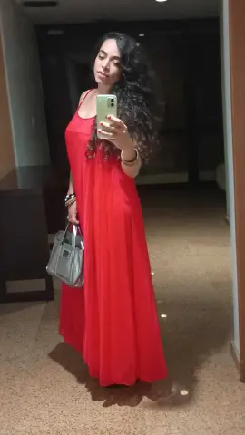 SweetsAnne poses in a long red dress, holding a silver handbag and a phone for a mirror selfie with her long, dark curly hair.