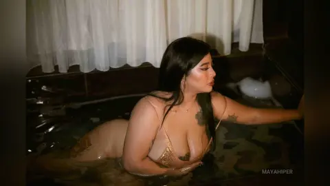 Curvy woman in a beige bikini relaxing in a dark, moody indoor pool with soft curtain lighting.