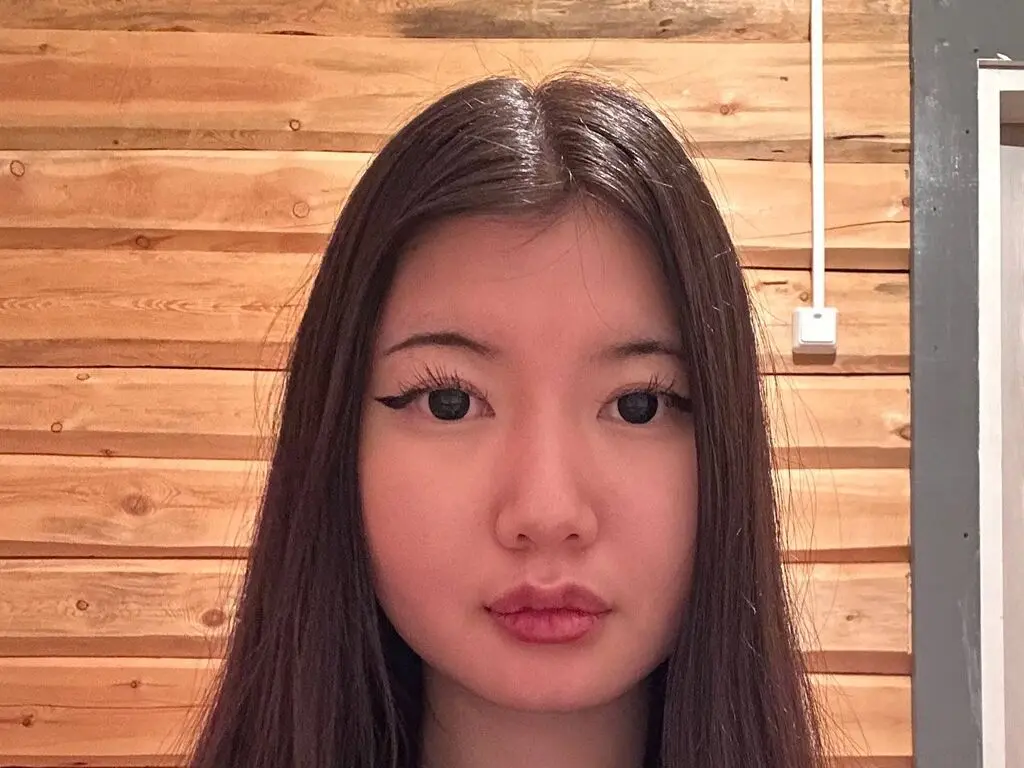 Young woman with long dark hair looking at camera against a warm wooden plank wall background.