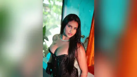 Glamorous woman in a black corset outfit posing in a teal room with a moody, cinematic aesthetic.