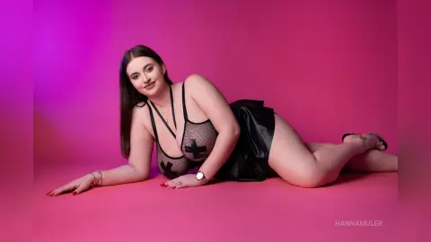Smiling woman in black mesh lingerie and skirt posing on a vibrant pink studio background.