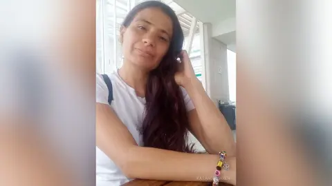 Smiling woman in a white t-shirt relaxing indoors with long dark hair and colorful beaded bracelets.