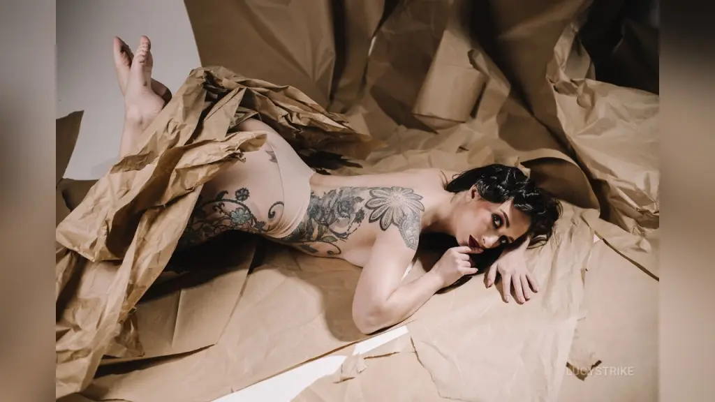Tattooed woman lying on crumpled brown paper in moody, dramatic low-light lighting.