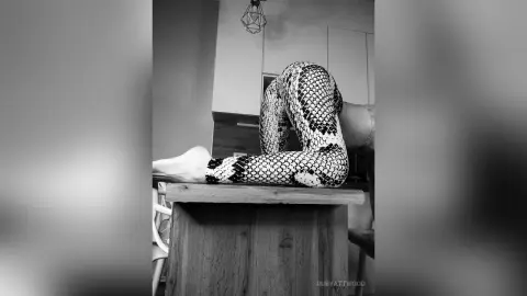 RubyAttwood arches her back while wearing patterned leggings, resting her feet on a wooden table in a black and white photo.