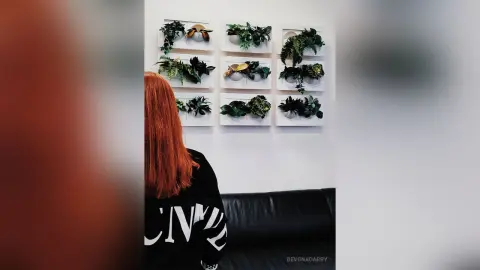 Red-haired woman in a black sweatshirt looking at modern botanical wall art in a minimalist living room.